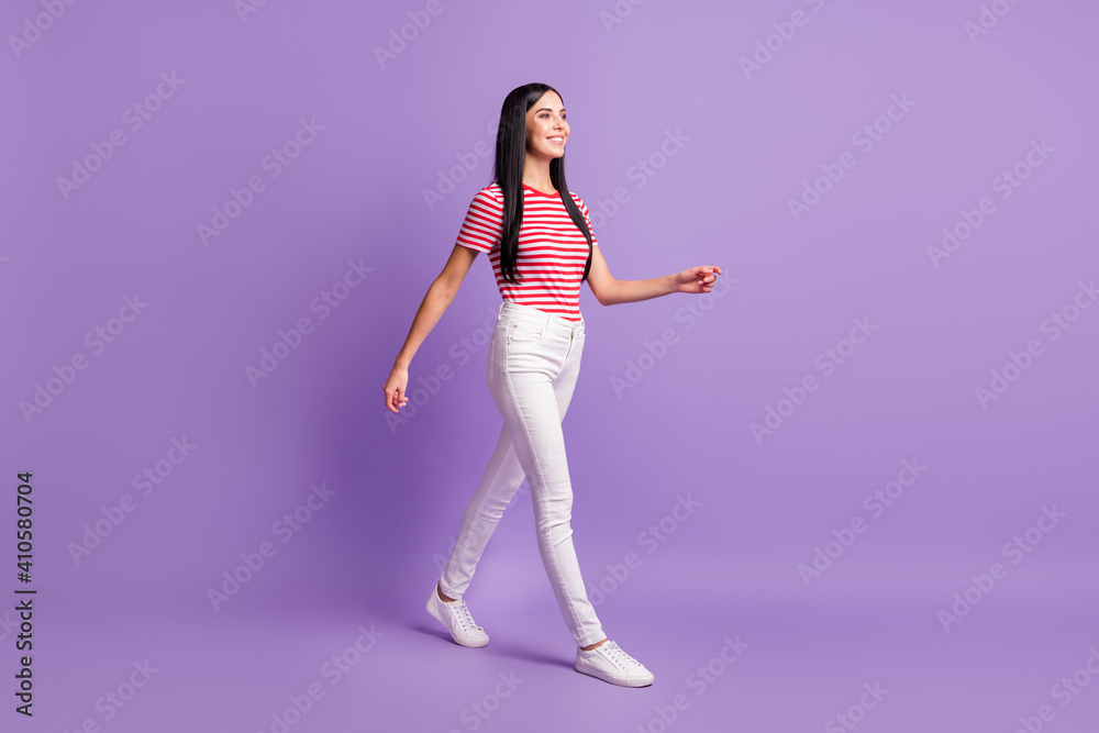 Full length profile side photo of happy brown haired young woman look walk empty space isolated on purple color background Full length profile side photo of happy brown haired young woman look walk empty space isolated on purple color background