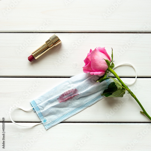 Fototapeta Naklejka Na Ścianę i Meble -  Top view arrangement with lipstick, rose, medical mask with lipstick trace on white wooden background