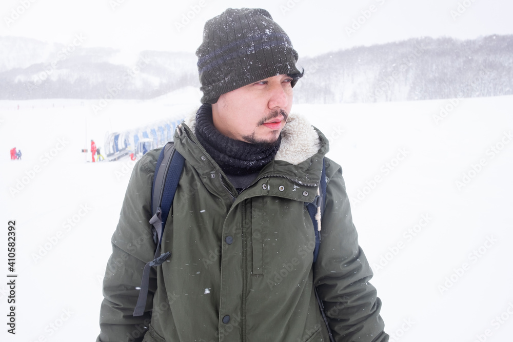 Asian man wearing a sweater jacket stands in a ski resort. In the middle of the snow mountain.. Asian man wearing a sweater jacket stands in a ski resort. In the middle of the snow mountain..