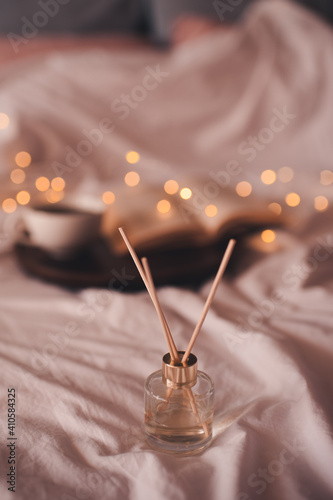 Liquid home perfume in glass bottle with sticks over glowing lights in bed at home close up. Cozy atmosphere concept. Freshness.