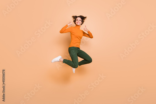 Full size photo of young happy excited positive cheerful girl jumping showing thumb-up isolated on beige color background