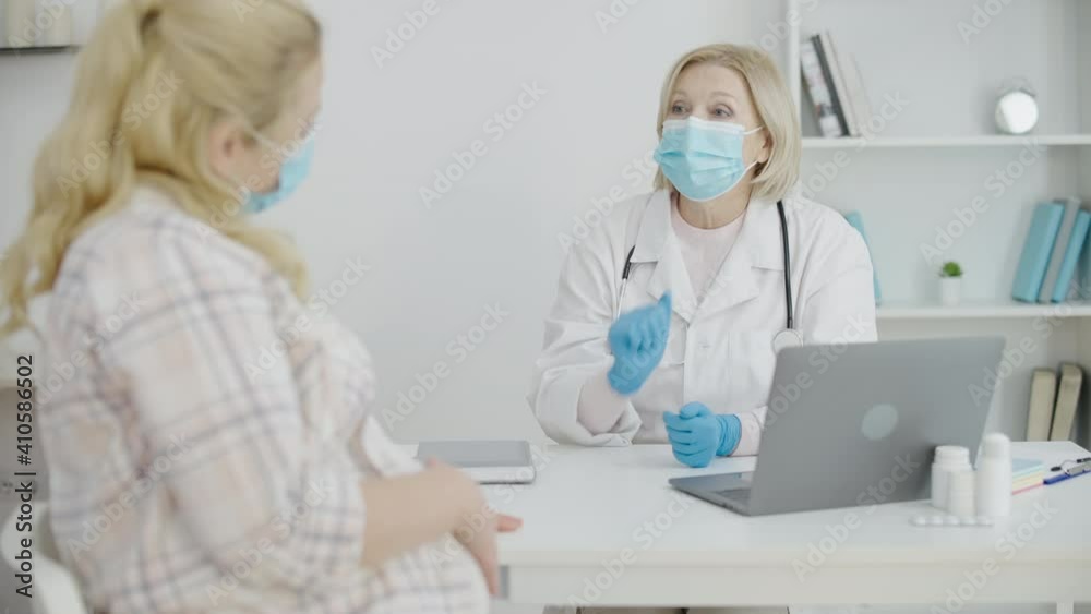 Obstetrician in mask and gloves talking to patient, pregnancy during coronavirus Obstetrician in mask and gloves talking to patient, pregnancy during coronavirus
