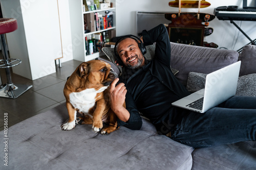 Middle aged man relaxing on the sofa and watching a movie next to his dog