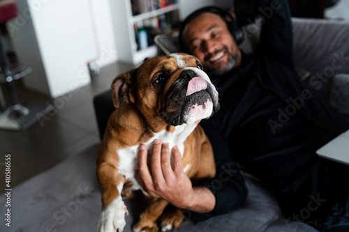 Middle aged man relaxing on the sofa and listening to music next to his dog