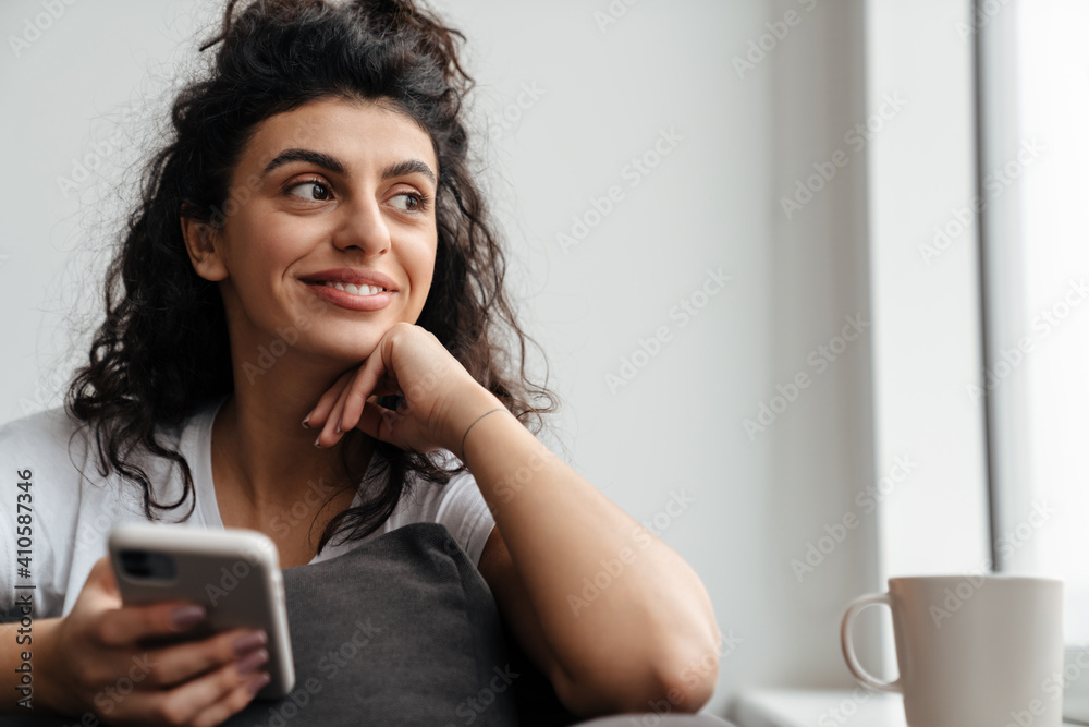 Happy brunette young woman using mobile phone while sitting on sofa Happy brunette young woman using mobile phone while sitting on sofa
