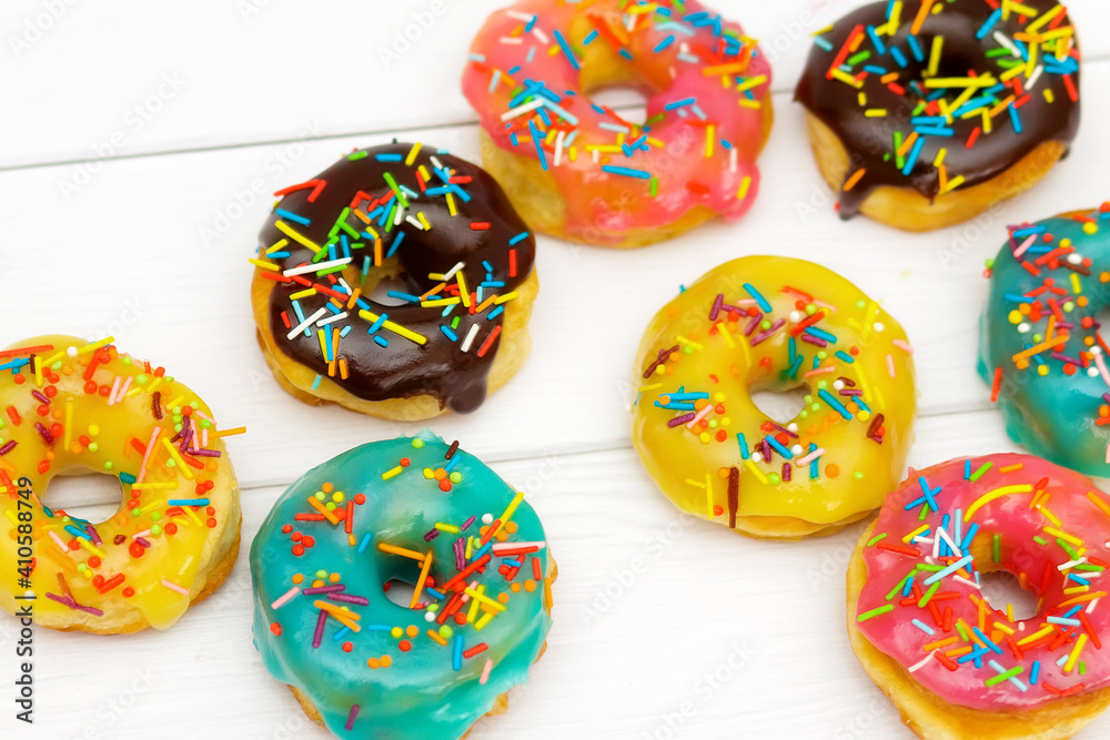 Homemade donuts with pink, blue, yellow and chocolate glaze with multicolored sugar sprinkles on a white wooden background. Bright background, selective focus
