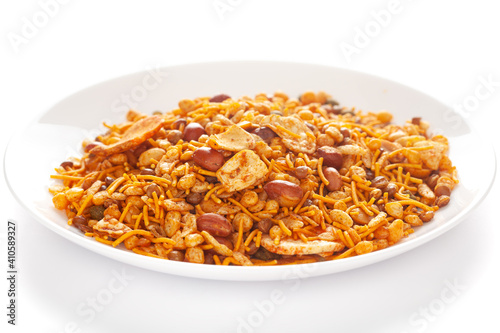 Hot spicy NavRatan snacks in a white ceramic plate, made with red chili, peanuts, corn flakes, etc. Pile of Indian spicy snacks (Namkeen), under backlight, side view