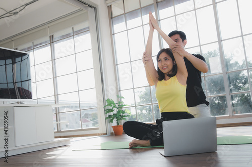 Asian young beautiful  woman practicing Yoga by stretching arm with a man trainer in living room at home, healthy Indoor sports activity