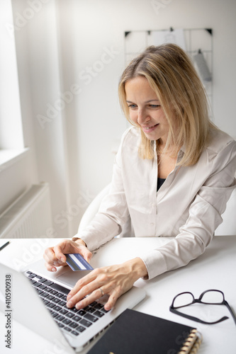beautiful, blond businesswoman doing online shopping with her credit card in her office with her laptop and is happy