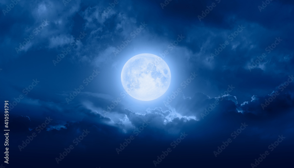 Night sky with full bright moon in the clouds, blue sea in the foreground 