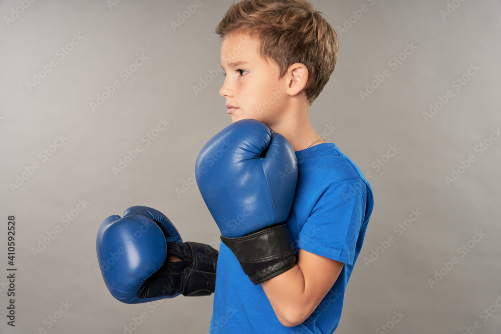 Adorable boy in boxing gloves standing against gray background Adorable boy in boxing gloves standing against gray background