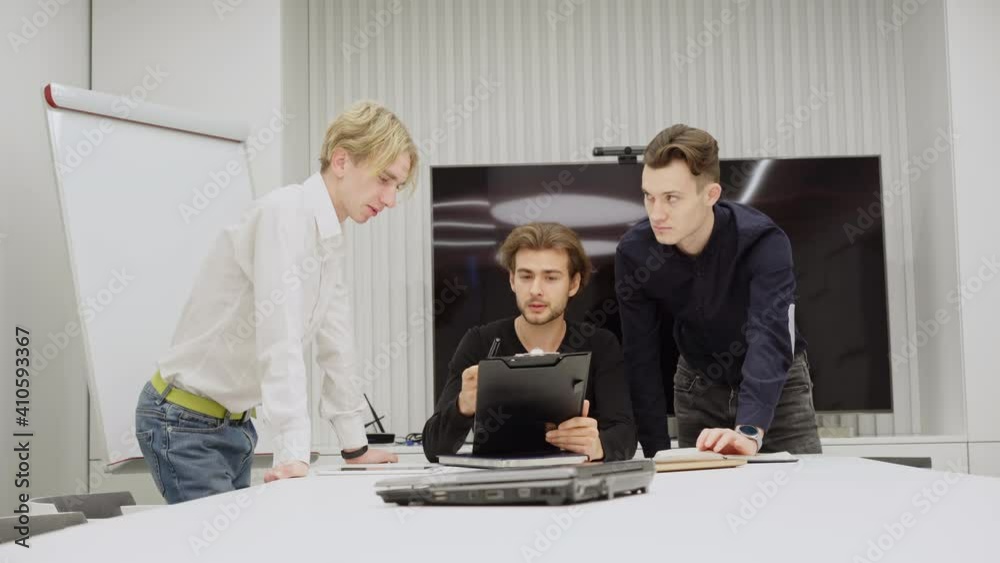 Young millennial coworkers discussing project indoors in conference room. Successful Caucasian handsome men talking in office. Startup and teamwork concept. Young millennial coworkers discussing project indoors in conference room. Successful Caucasian handsome men talking in office. Startup and teamwork concept.