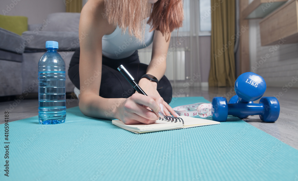Young woman sitting in mat writes training plans at home. - obrazy, fototapety, plakaty 