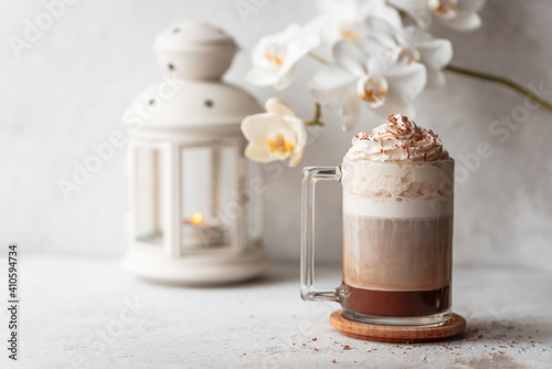 Hot latte macchiato with delicious foam in a tall transparent glass on an easy table setting. Photo in a high key. Breakfast time. Rustic background.