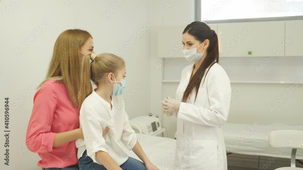 Female doctor preparing child before making injection, consulting. Girl sits with mother in hospital listening to nurse talks. Female doctor preparing child before making injection, consulting. Girl sits with mother in hospital listening to nurse talks.