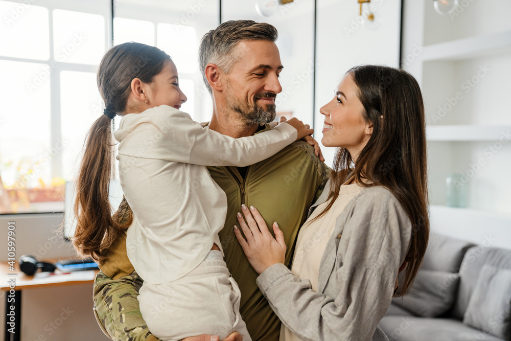 Happy masculine military man smiling and hugging his family indoors - obrazy, fototapety, plakaty 