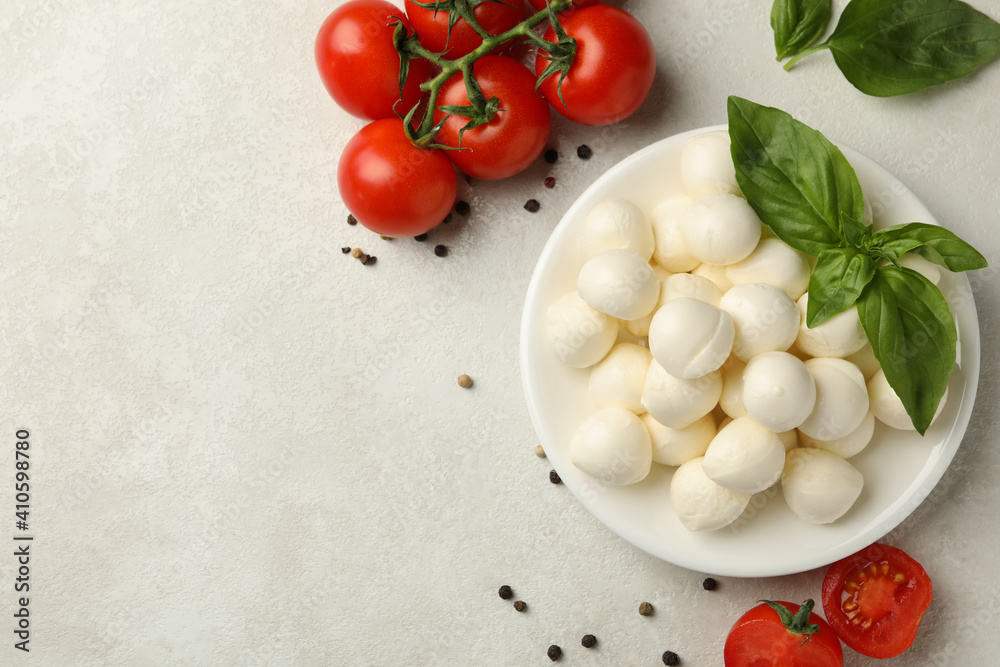 Plate with mozzarella and basil, tomato and pepper on white textured background, space for text Plate with mozzarella and basil, tomato and pepper on white textured background, space for text