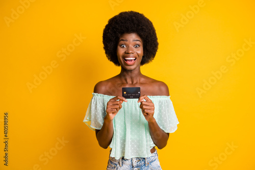 Photo portrait of excited woman holding credit card in two hands isolated on vivid yellow colored background