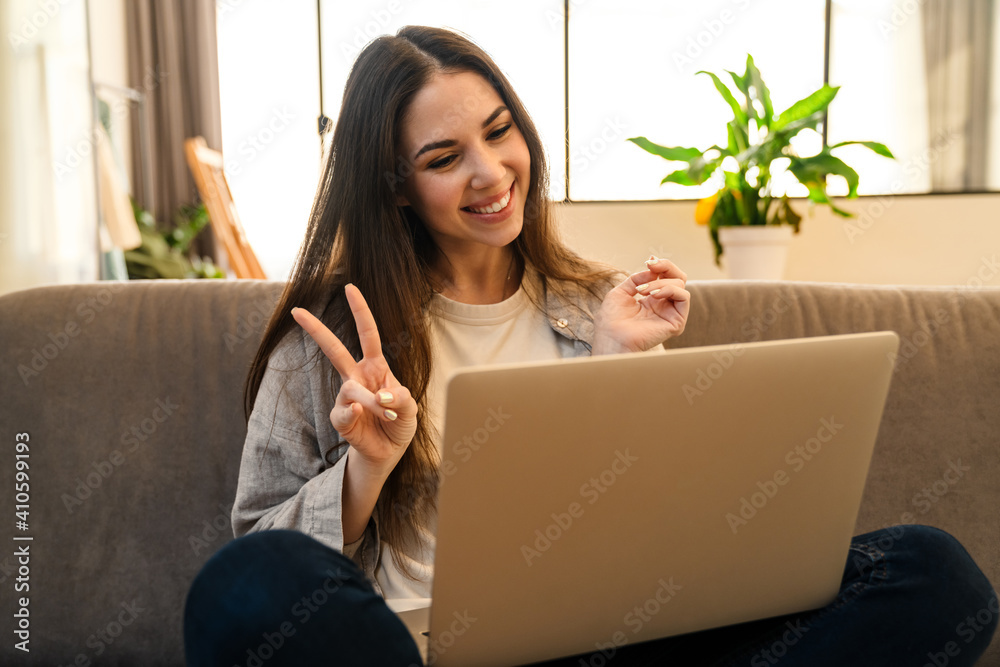 Happy young woman gesturing peace sign while using laptop Happy young woman gesturing peace sign while using laptop