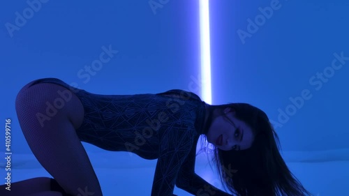 Seductive brunette enjoys dancing strip in dark studio against background of bright neon lights. Stripper arches her gorgeous body, sexually spreads her legs and spins on floor. Close up. Slow motion. photo