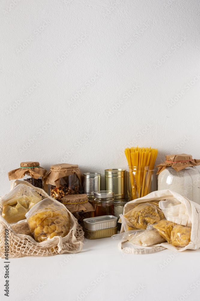 Fototapeta premium Necessary food for the period of quarantine and isolation, the concept of staying at home, canned food and bags of cereals, various pasta and flour, sugar and honey and coffee