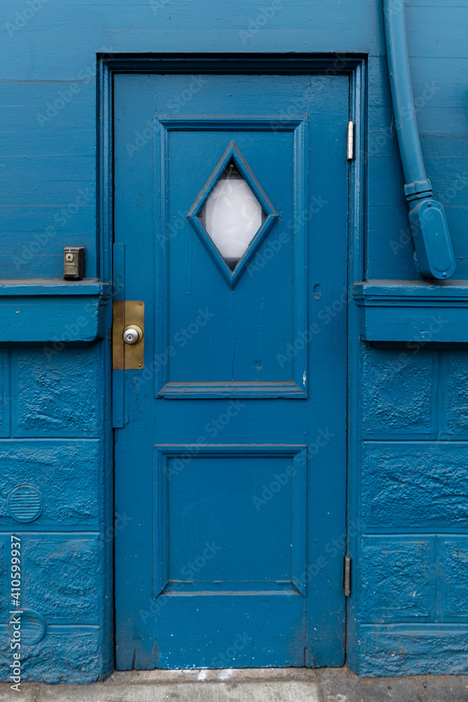 Vertical shot of blue door against a blue painted wall - obrazy, fototapety, plakaty 