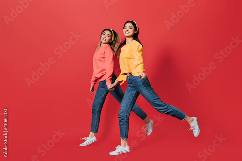 Happy girls in jeans and sweaters move on red background