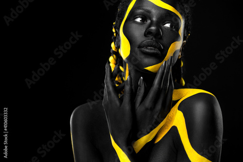 Yellow and black body paint. Woman with face art. Young girl with colorful bodypaint. An amazing afro american model with makeup. photo