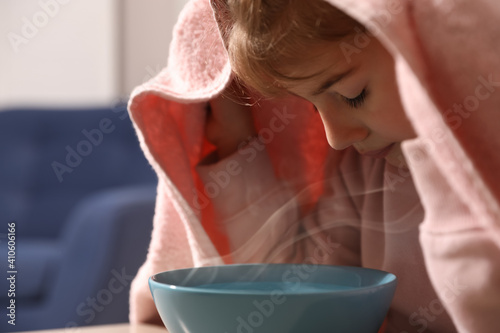 Little girl covering head with towel and inhaling steam indoors, closeup