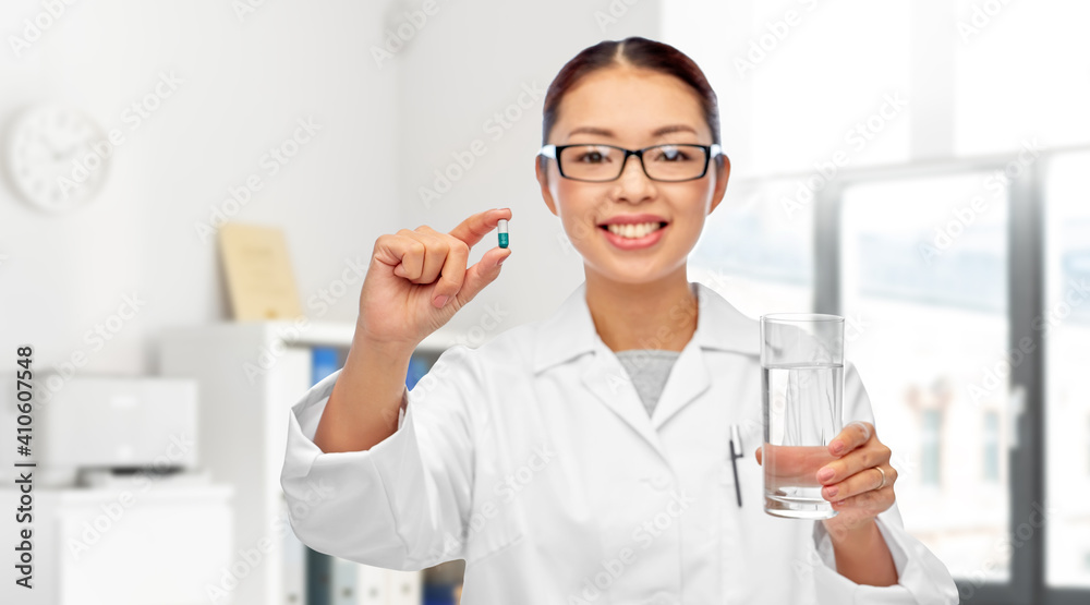 medicine, profession and healthcare concept - happy smiling asian female doctor or nurse pill and glass of water over medical office at hospital on background medicine, profession and healthcare concept - happy smiling asian female doctor or nurse pill and glass of water over medical office at hospital on background