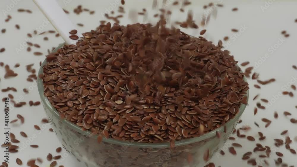 Close shot of dropping flax seeds over a glass bowl filled with flax seeds Close shot of dropping flax seeds over a glass bowl filled with flax seeds