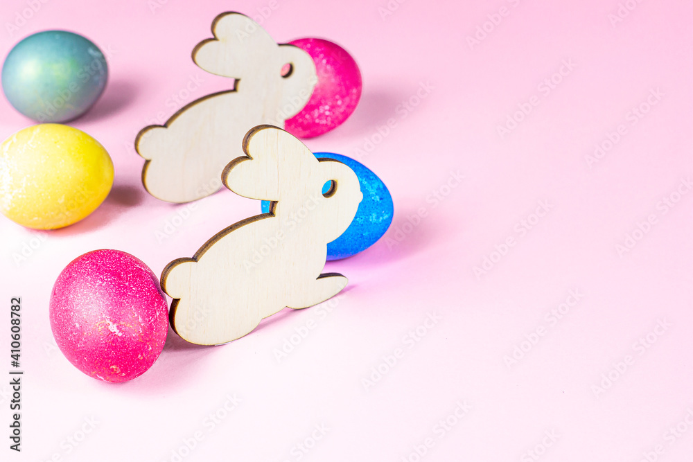 Funny wooden Easter Bunny with colorful eggs as symbols of a holiday with copy space on light pink background.