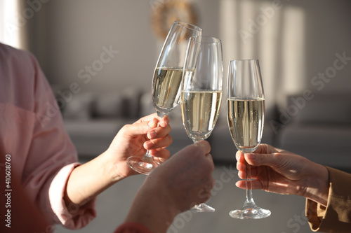People clinking glasses of champagne in living room, closeup. Holiday cheer and drink