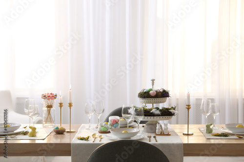 Beautiful Easter table setting with burning candles and floral decor indoors