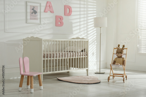 Comfortable crib near wall with pink letters in baby room. Interior design