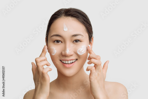 Beautiful young Asian woman gets cream in her face. The concept of skin care and hydration. a young woman with perfect clean skin health.