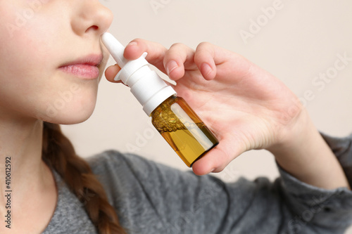 Sick little girl using nasal spray on beige background, closeup