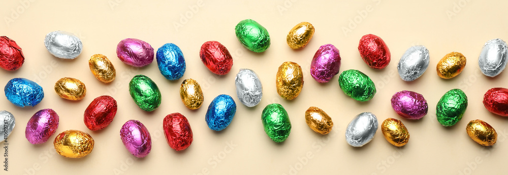 Chocolate eggs wrapped in colorful foil on beige background, flat lay. Banner design Chocolate eggs wrapped in colorful foil on beige background, flat lay. Banner design
