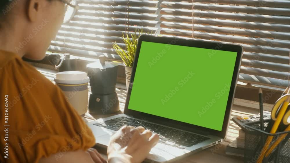Over the shoulder shot of a business woman working in office interior on pc on desk, looking at green screen. Office person using laptop computer with laptop green screen,
