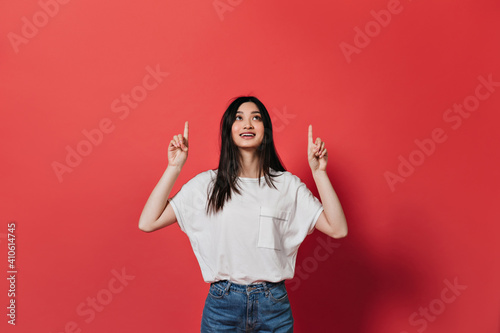 Positive woman in white t-shirt points fingers up and smiles