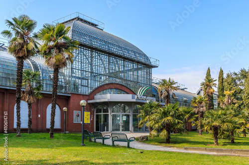 Buildings of palm garden in Frankfurt. Palm trees with meadow in front of the entrance. Glass roof with windows and bricks from the building. Path with benches and lamps photo