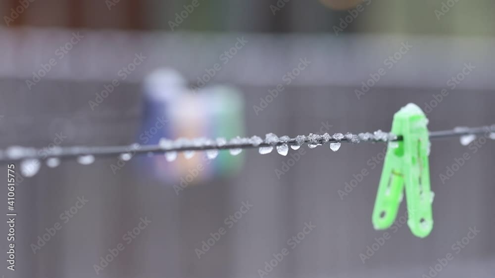 A green clothespin covered in ice and snow hangs on a wire on a cloudy cold day in soft focus. An icy clothespin sways in the wind with frozen water drops. Climatic icing. Frozen freezing rain. A green clothespin covered in ice and snow hangs on a wire on a cloudy cold day in soft focus. An icy clothespin sways in the wind with frozen water drops. Climatic icing. Frozen freezing rain.