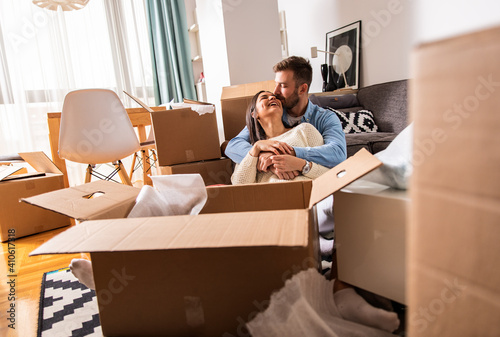 Smiling young couple move into a new home sitting on floor and unpacking boxes of their belongings.