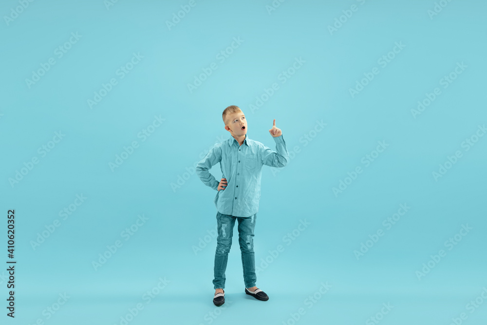 Pointing. Childhood and dream about big and famous future. Pretty little boy isolated on blue studio background. Childhood, dreams, imagination, education, facial expression, emotions concept. Pointing. Childhood and dream about big and famous future. Pretty little boy isolated on blue studio background. Childhood, dreams, imagination, education, facial expression, emotions concept.