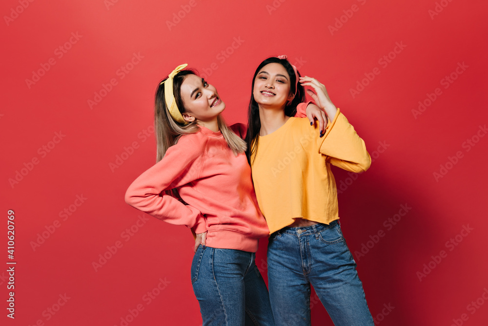 Beautiful Asian girls in sweaters and jeans posing on red background Beautiful Asian girls in sweaters and jeans posing on red background