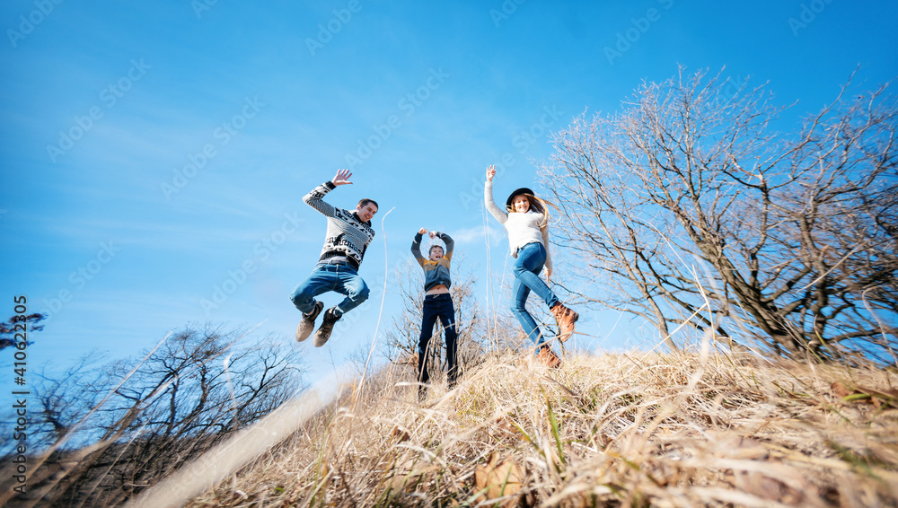 Happy cheerful smiling family jumping dancing on blue sky background in spring forest, wide angle image