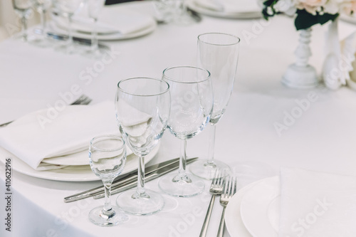 Fancy table set for dinner with napkin glasses in restaurant, luxury interior background. Wedding elegant banquet decoration and items for food arranged by catering service on white tablecloth table. © Юлия Завалишина