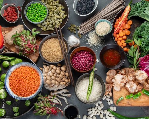 Asian raw vegan food, grain, seeds and vegetables on dark background