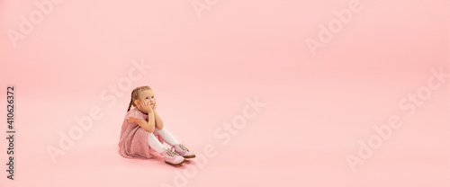 Dreamful baby. Childhood and dream about big and famous future. Pretty girl on coral pink studio background. Childhood, dreams, imagination, education, facial expression, emotions concept. Flyer