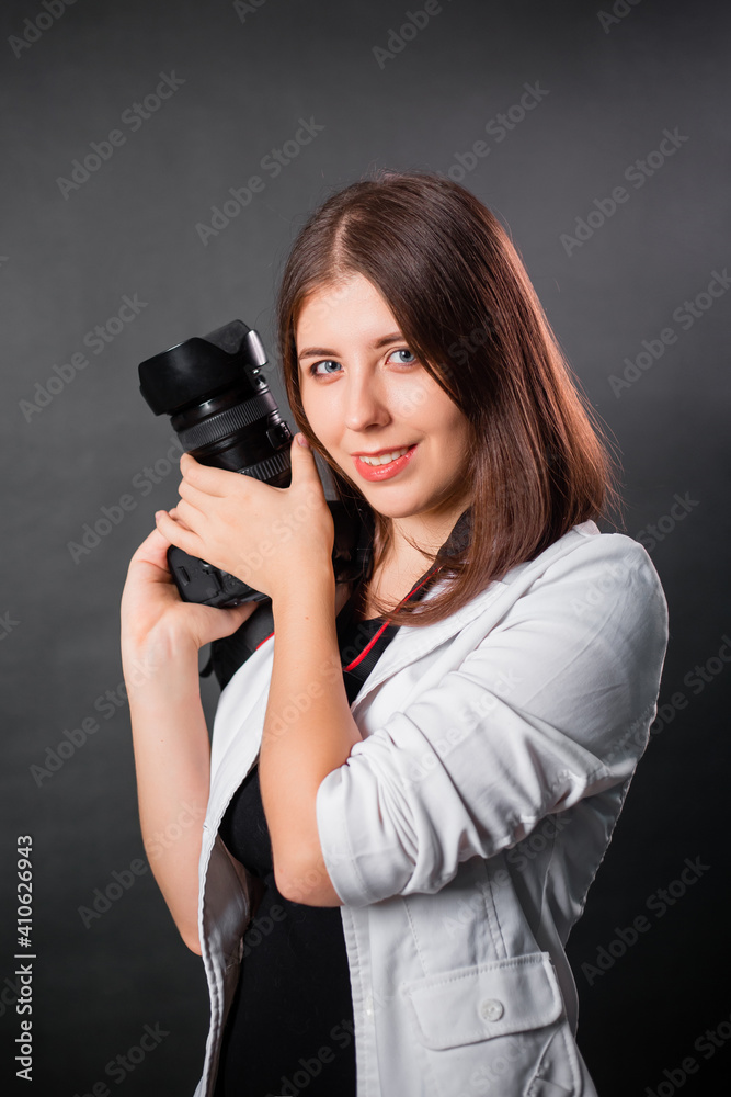 Woman photographer with a SLR camera in her hands posing on a gray background.